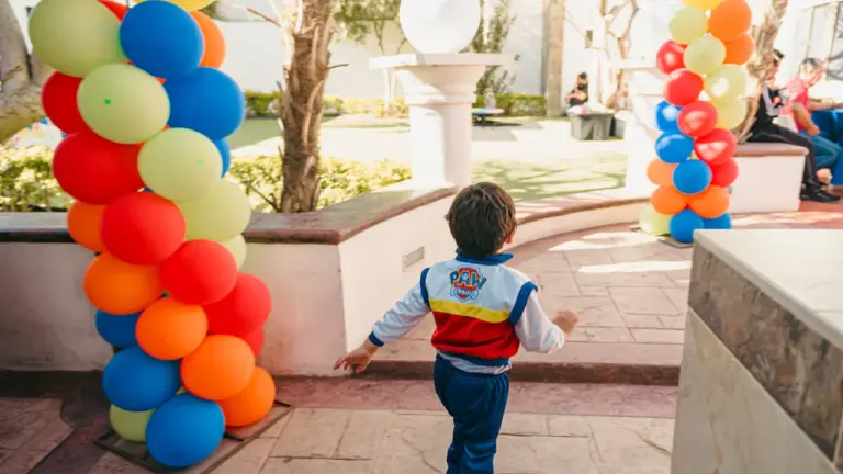 Un jeune garçon en veste colorée court vers des décorations de ballons festifs.