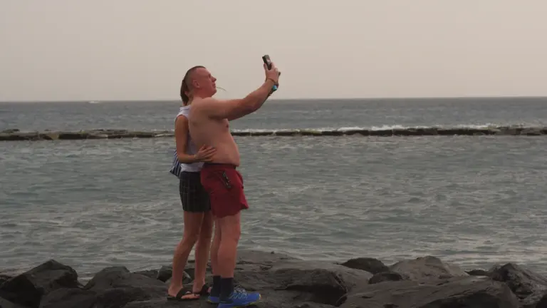 Un couple prend un selfie sur une plage rocheuse au bord de la mer.