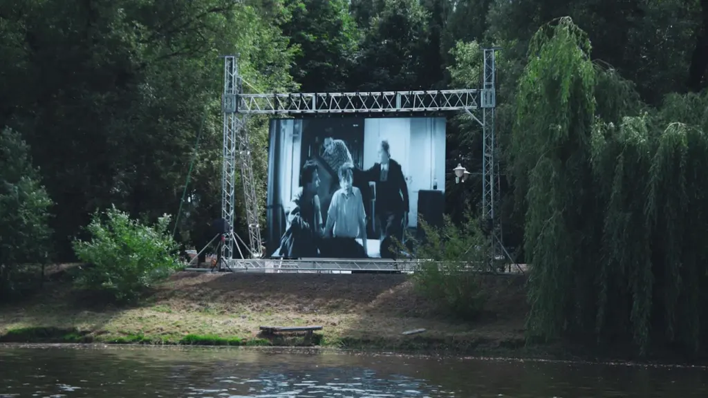 Grand écran de cinéma en plein air installé dans un parc verdoyant près de l'eau.