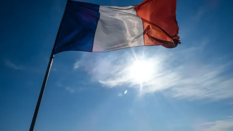 Drapeau français flottant sous un soleil éclatant dans un ciel bleu dégagé.