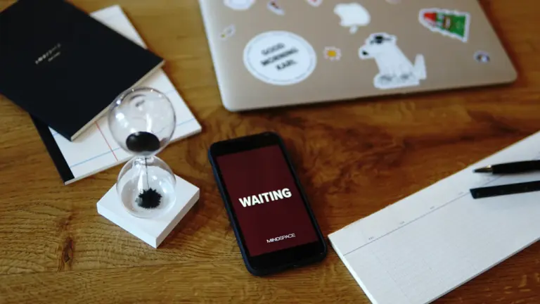 Smartphone affichant le mot waiting sur un bureau avec un sablier et cahiers.