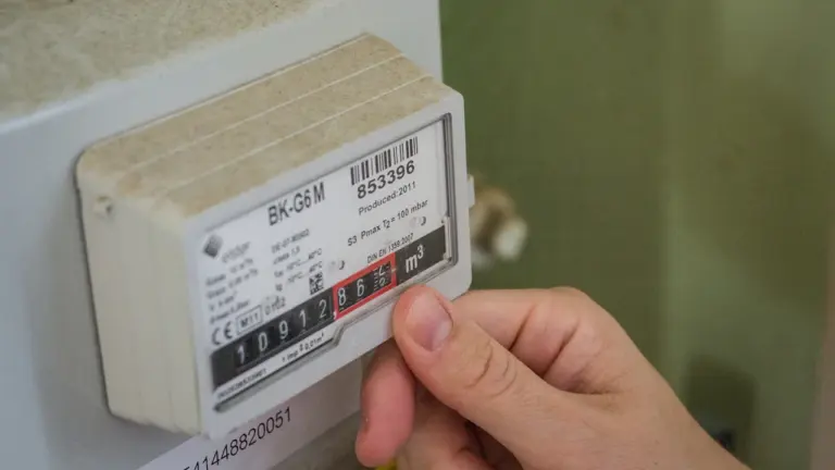 Une main vérifie un compteur électrique résidentiel pour surveiller sa consommation d'énergie.