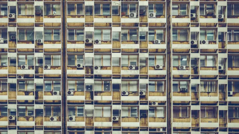 Façade d'un immeuble résidentiel avec de nombreuses unités de climatisation individuelles aux fenêtres.