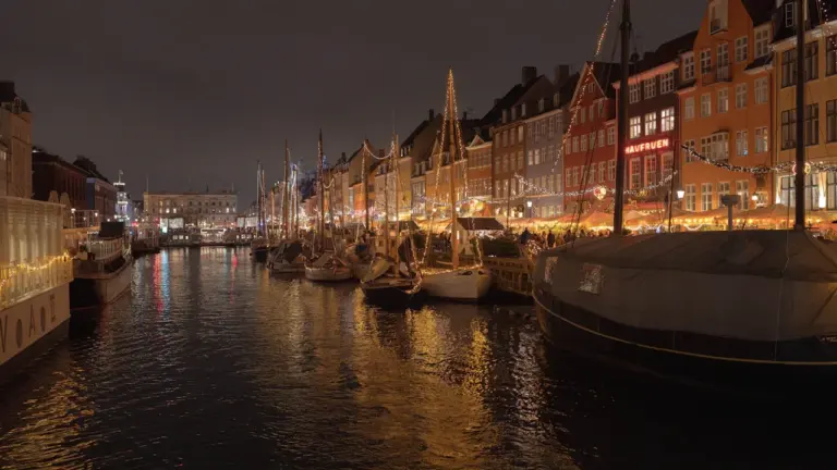 Un canal européen bordé de bateaux et de bâtiments illuminés à la tombée de la nuit.