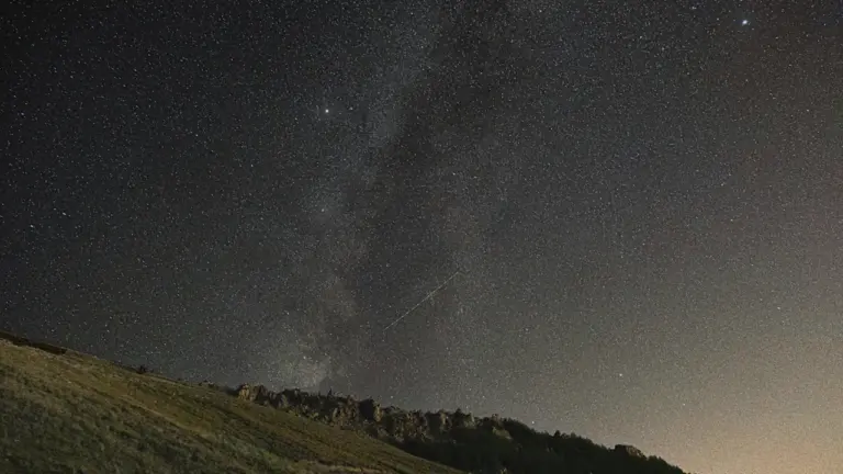 Ciel étoilé nocturne au-dessus d'une colline herbeuse, parfait pour observer les étoiles filantes.