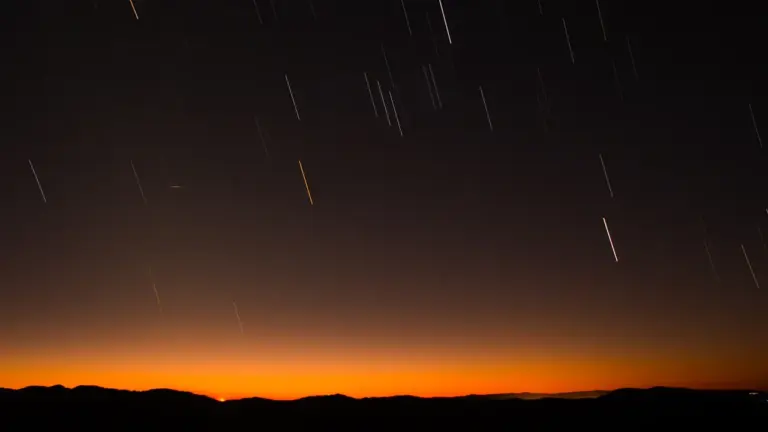 Traces d'étoiles filantes illuminant le ciel nocturne au-dessus d'une silhouette de collines sombres.