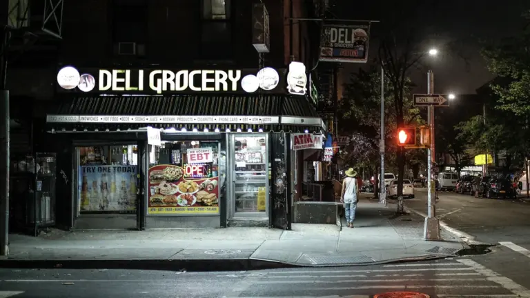Une épicerie de quartier en France illuminée la nuit au bord de la rue.