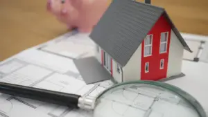 Maquette de maison rouge et blanche avec une loupe d'analyse immobilière.