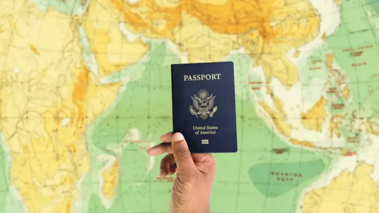 Une main tient un passeport au-dessus d'une carte du monde dépliée.
