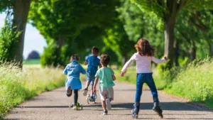 Des enfants jouant dehors sur des trottinettes et rollers en milieu urbain.