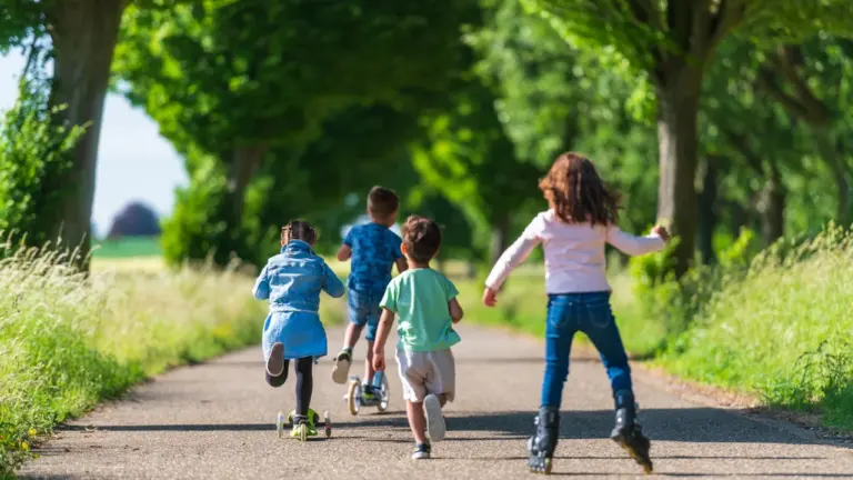 Des enfants jouant dehors sur des trottinettes et rollers en milieu urbain.