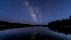 Voie lactée se reflétant sur un lac de montagne sous un ciel étoilé nocturne.