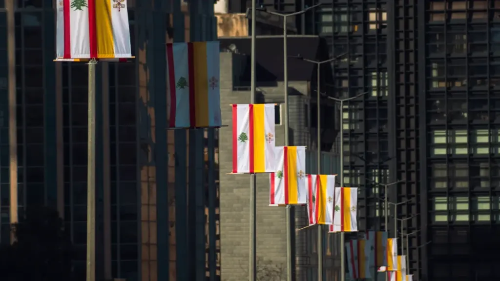 Des drapeaux alignés flottant devant une architecture urbaine pour une commémoration solennelle.