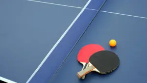 Deux raquettes de tennis de table et une balle sur une table bleue.