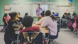 Des élèves en classe écoutant leur professeur devant un tableau blanc interactif.